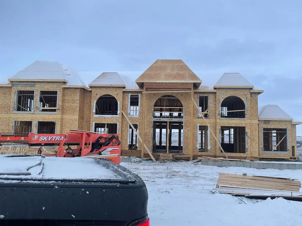 A large custom home framed and sheathed in winter with a telehandler on site